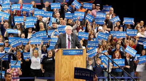 Bernie Sanders speaking at a rally, with a crowd of supporters in the background